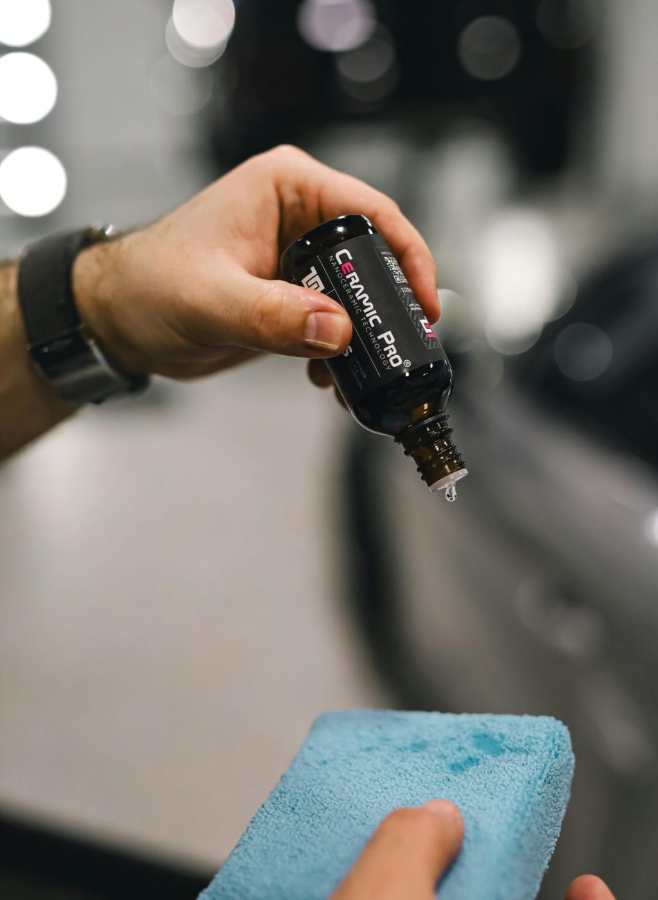 Close-up of hands applying ceramic coating on car with blue sponge.